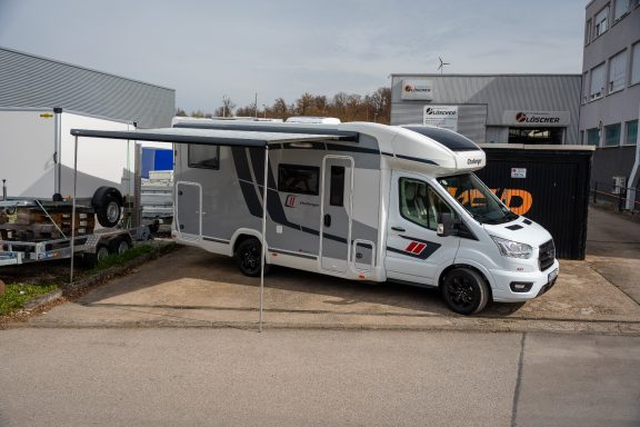 Weißer Wohnmobil mit Markise, parkt an einer Werkstatt.